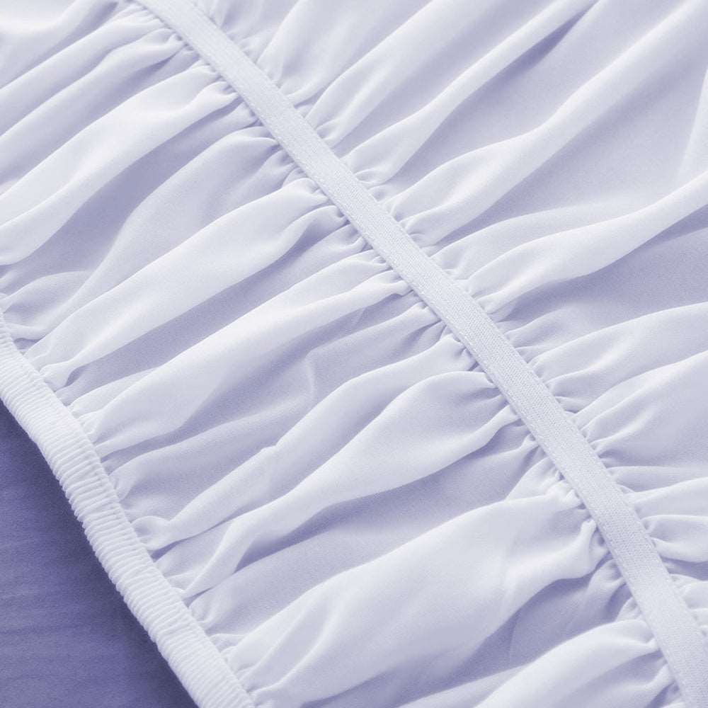 Elastic band wrap around white bed skirt without surface couvre lit.